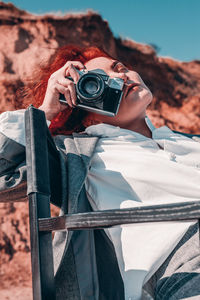 Female model photographing while sitting on chair against rock formations