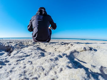Rear view of man on beach against clear blue sky