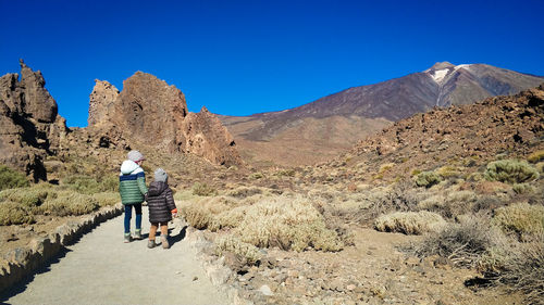 Rear view of man walking on mountain against clear blue sky