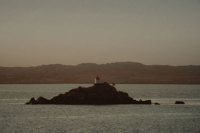 Lighthouse by sea against sky during sunset