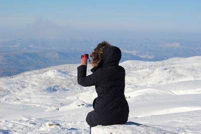 Rear view of person photographing on snowcapped mountain