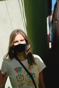 Portrait of young woman with coronavirus mask standing against wall