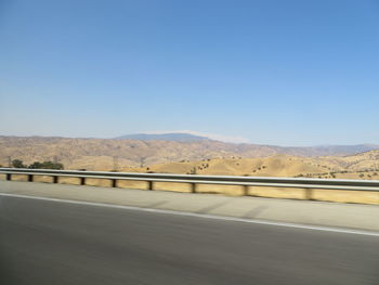 Road leading towards mountains against clear blue sky