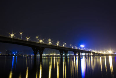 Illuminated bridge over river against sky at night
