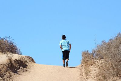 Rear view of man walking on landscape against clear blue sky