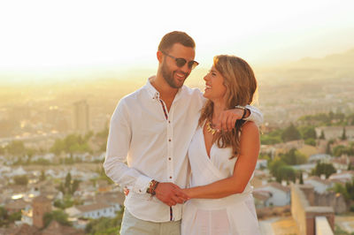 Smiling couple standing against cityscape during sunset