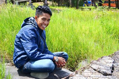 Portrait of smiling young man sitting by grass