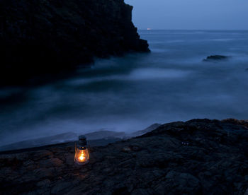 Illuminated rocks by sea against sky at dusk