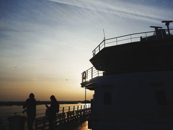 Silhouette people standing by railing against sky during sunset