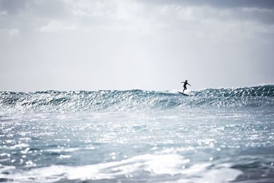 Silhouette man surfing in sea against sky