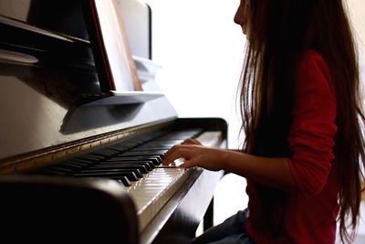 Side view of girl playing piano at home