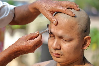 Cropped hand of man cutting eyebrow of monk during ordination