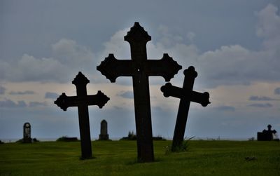 Cross in cemetery against sky