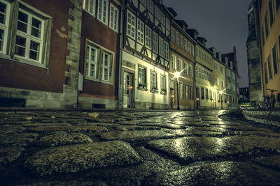 Surface level of wet street amidst buildings at night