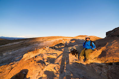 Woman sitting on rock formation against clear sky