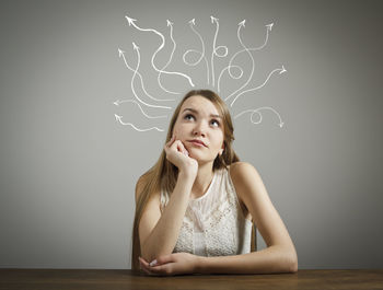 Portrait of beautiful young woman sitting on table against wall