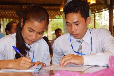 Teenage girl with friend writing on note pad at table