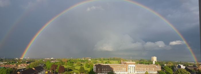 Rainbow over trees against cloudy sky