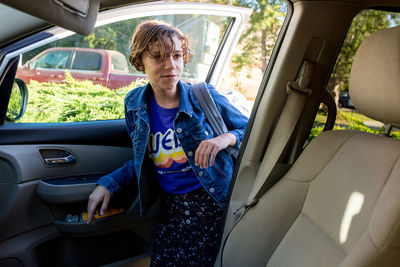 Teen girl with short hair gets into the car with her backpack