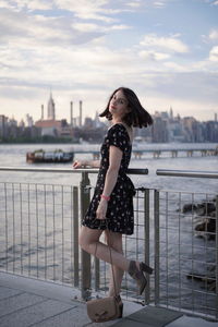 Portrait of woman standing against railing against sky