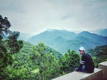 Man sitting on mountain against sky