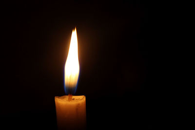 Close-up of burning candle against black background