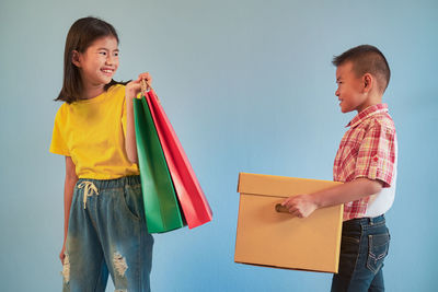 Smiling boy and girl holding shopping bags and container against colored background