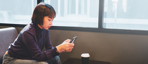 Young man using mobile phone while sitting on window