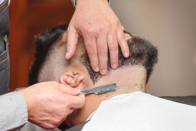 Cropped hands of barber shaving customer beard in salon