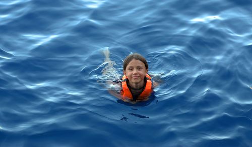 The girl in a life jacket floats in the sea