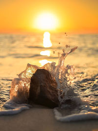 Close-up of surf splashing on rock at beach during sunset