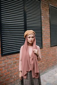 Portrait of young woman standing against brick wall