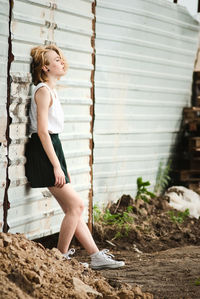 Side view of woman leaning on corrugated wall