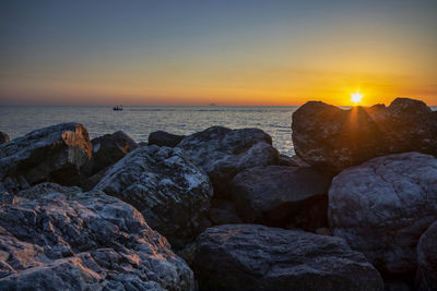 Rocks on beach against sky during sunset