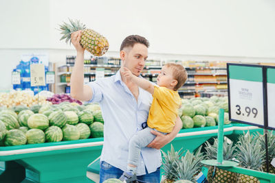Man with son holding pineapple at supermarket
