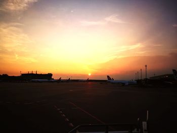 Silhouette airplane on airport runway against sky during sunset