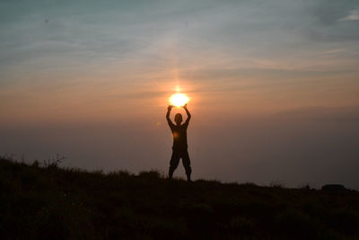 Silhouette man standing on field against sky during sunset