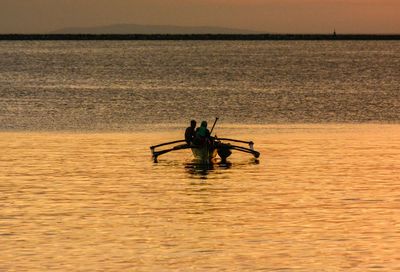 Silhouette people rowing boat sailing on sea against sky during sunset