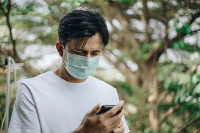 Man using mobile phone while wearing mask against trees