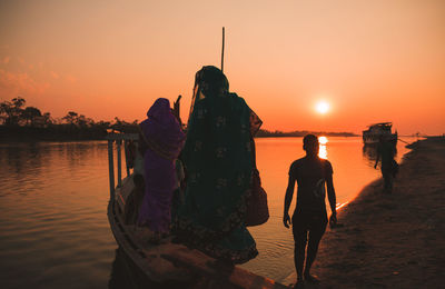 Rear view of people at beach during sunset