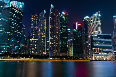 Illuminated modern buildings in city against sky at night