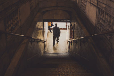 Rear view of man walking in illuminated tunnel