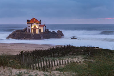 Lighthouse on beach by sea against sky