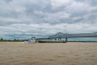 Tugboat pushing barge on the muddy mississippi river. crescent city bridge in background