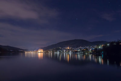 Illuminated city by sea against sky at night