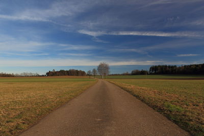 Road amidst field against sky