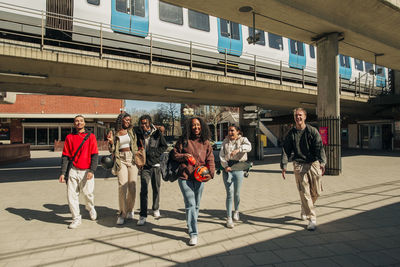 Happy multiracial young friends walking together on street below bridge