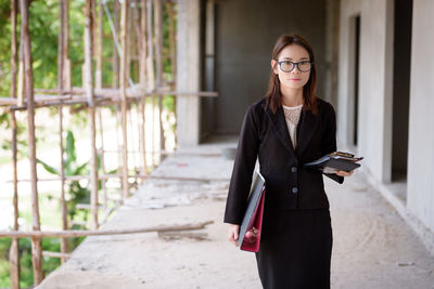 Portrait of young businesswoman with file standing in incomplete building at construction site