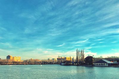 Sea by cityscape against sky during sunset