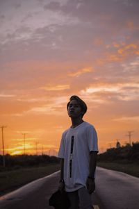 Portrait of boy standing on road against sky during sunset